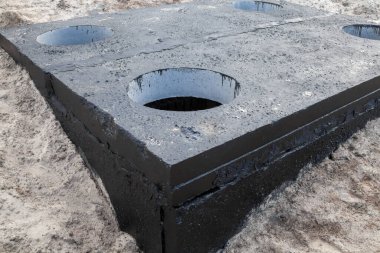 Beton bloktaki rögar kapağı siyah kömür katranıyla boyanmış. İnşaat alanı.