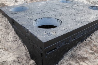 Manhole in the concrete block painted with black coal tar. Construction site. clipart