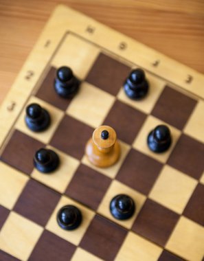 Siyah piyonlarla çevrili beyaz papaz. Satranç tahtasındaki tahta satranç taşları. Satranç oyunu. Üst görünüm.