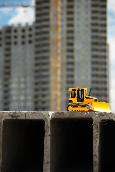 Toy bulldozer on the concrete block in the construction site. Building and architecture.