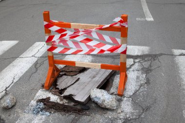 Yolda yaya geçidinde çukur var. Çukurun üstünde güvenlik şeridi olan ahşap güvenlik duvarı..