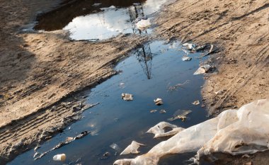 Çamurda çöp ve toprak yolda su birikintileri. Çevre kirliliği.