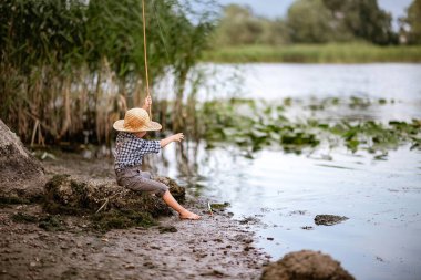            Hasır şapkalı küçük çocuk yazın nehirde oltayla balık yakalar. 