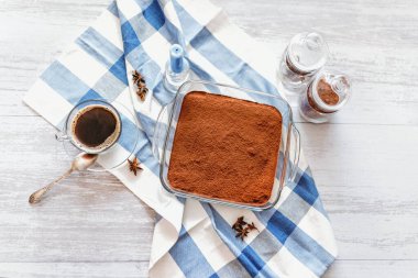 Üzerinde kakao tozu, mum ve bir fincan kahve serpilmiş tiramisu keki.