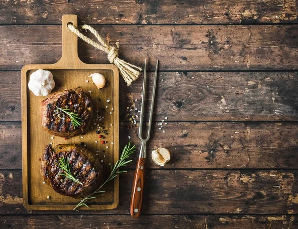 Grilled marbled meat steak Filet Mignon, seasonings, fork, wooden cutting board. Space for text. Juicy meat steak. Beef steak grilled/fried. Top view. Prepared meat steak. Close-up. Rustic background