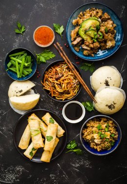 Asya çeşitli gıda kümesi, karanlık rustik taş arka plan. Çin yemekleri. Çin kizartma noodles, et, dim sum, kızarmış Bahar rulolar, Asya pirinç Çince buns atmak. Üstten görünüm. Asya stile akşam yemeği