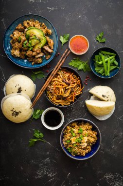 Asya çeşitli gıda kümesi, karanlık rustik taş arka plan. Çin yemekleri. Çin kizartma noodles, et, dim sum, kızarmış Bahar rulolar, Asya pirinç Çince buns atmak. Üstten görünüm. Asya stile akşam yemeği