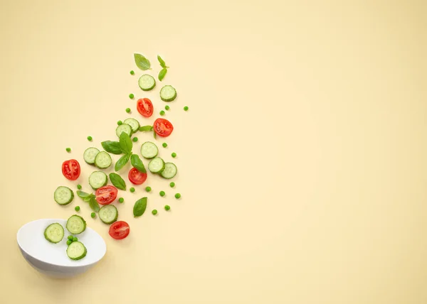 Fresh cut salad ingredients falling into white bowl on pastel yellow minimal background. Ingredients for making healthy vegetable salad. Dieting and clean eating concept layout with space for text