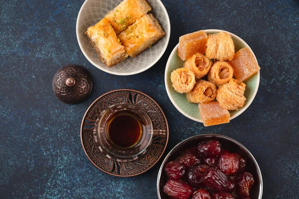 お菓子 バクラバ 上記からのルックと伝統的なアラブの新鮮な熱いお茶の時間 青い素朴な背景にトルコ料理とアラビア菓子とラマダーンスナックトップビュー ロイヤリティフリーのストック画像