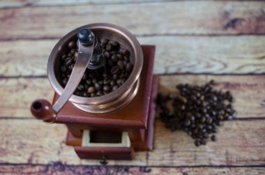 Kavrulmuş kahve çekirdekleri masaya saçılmış ve bakır kahve öğütücüsü ile ahşap bir çanta.