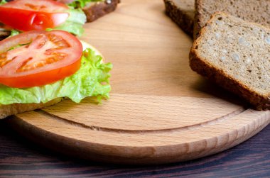 Karanlık bir masanın üzerinde kesme tahtasında ev yapımı sandviçler.