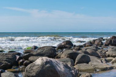 Taşlarla kaplı plaj manzarası. Mavi su. Bulutlu gökyüzü arkaplanı.