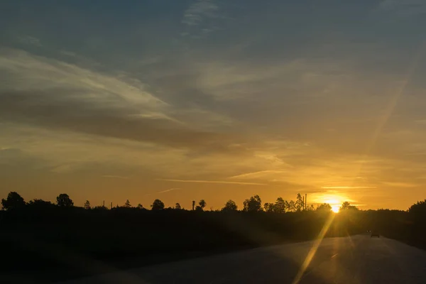 Sunrise over road with traffic. Car silhouette. Orange sun.