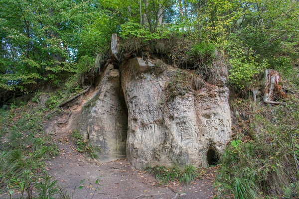 Sandstone cliff formation with caves in green forest. Text, names carved in wall