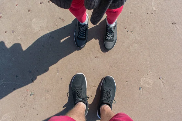 A view from above on the legs of a man and a woman standing opposite each other on a beach sand in summer