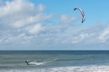 Liepaja, Letonya - 29 Eylül 2019: Kiteboardcu uçurtma atleti denizde uçurtma uçururken havada zıpladı. Mavi, bulutlu gökyüzü arkaplanı.