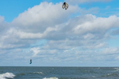Liepaja, Letonya - 29 Eylül 2019: Kiteboardcu uçurtma atleti denizde uçurtma uçururken havada zıpladı. Mavi, bulutlu gökyüzü arkaplanı.