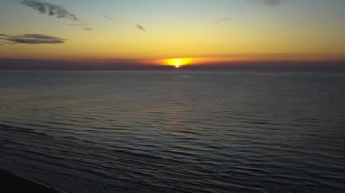 Güzel bir günbatımında deniz üzerinde uçan bir dron. Deniz yüzeyinde gün batımı dalgalarla, hava görüntüleriyle.