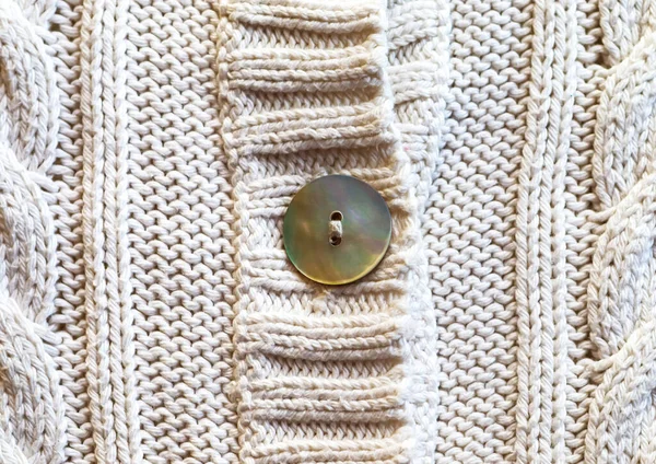 Detail of knitted white cotton with mother of pearl button. Knitting fabric cotton.