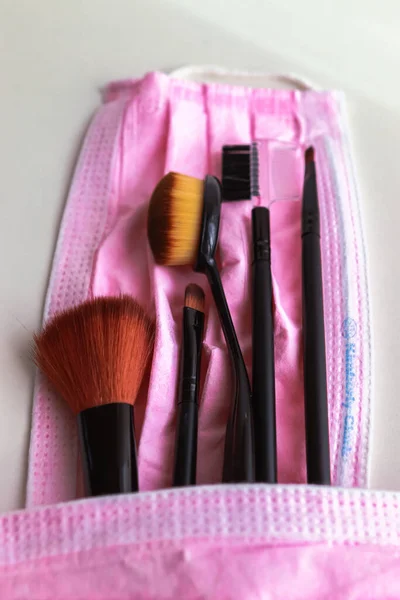 Profesyonel makyaj fırçası beyaz arka planda koruyucu pembe tıbbi maskeyle örtülmüş. Fırça seti beyaz arkaplanda izole edildi