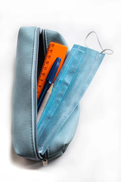 Beyaz arka planda koruyucu yüz maskesi olan kalem kutusu. Coronavirus konsepti. Okul temasına dönelim. Coronavirus konsepti