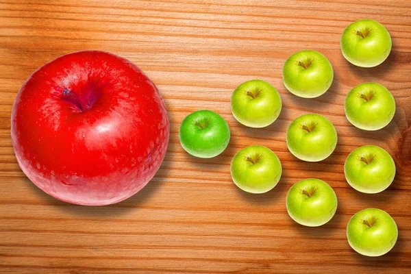 Big red apple and group of ordered green apples on striped wooden desk