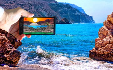 Afrodit 'in doğduğu yerin yakınlarındaki insan eli ve akıllı telefonlu hayali manzaranın canlı bir görüntüsü. 