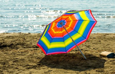 Kıbrıs Rum Kesimi Larnaka 'daki sıcak Akdeniz' in arka planında kumsalda gökkuşağı şemsiyesi
