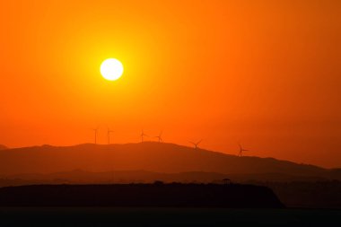 Yazın Kıbrıs Rum Kesimi 'ndeki kuru tuz gölü üzerinde günbatımının arka planında rüzgar jeneratörleri