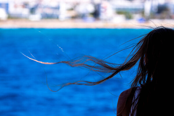 Nice girl head and windy hair silhouette on the blurred background of blue sea 