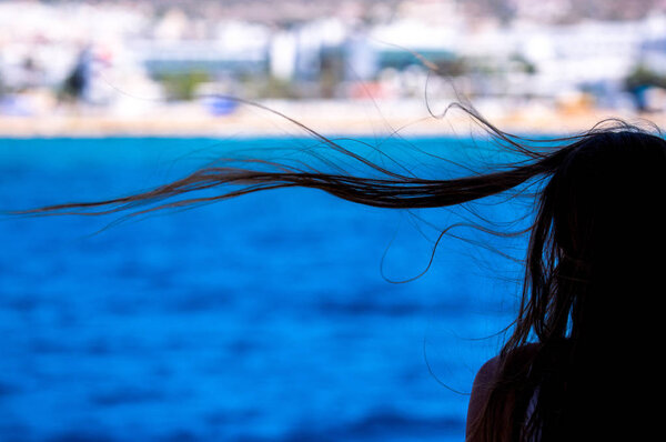 Nice girl head and windy hair silhouette on the blurred background of blue sea 