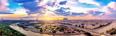Moskova üzerindeki günbatımının geniş açılı panoramik görüntüsü. Şehir nehri, gezici tekneler ve köprü üzerindeki bulut yansımaları.