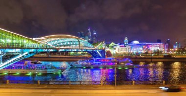 Moskova nehri boyunca asılı köprünün altından geçen aydınlık teknelerin uzun ve parlak yolları.