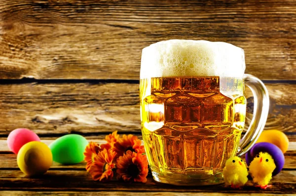 Glass of cold light beer with Easter decorations on a wood backg