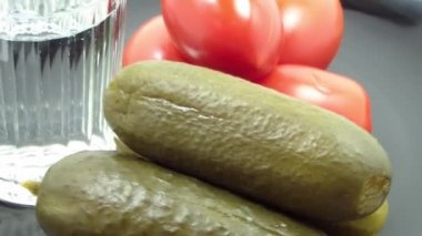 A big glass of vodka, cucumbers and tomatoes in a plate