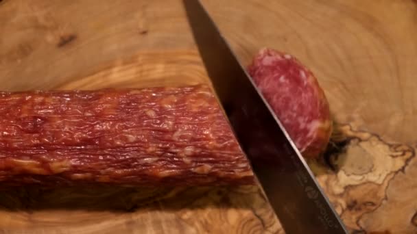 A man cuts a cured sausage with a sharp knife on a wooden board — Stock Video