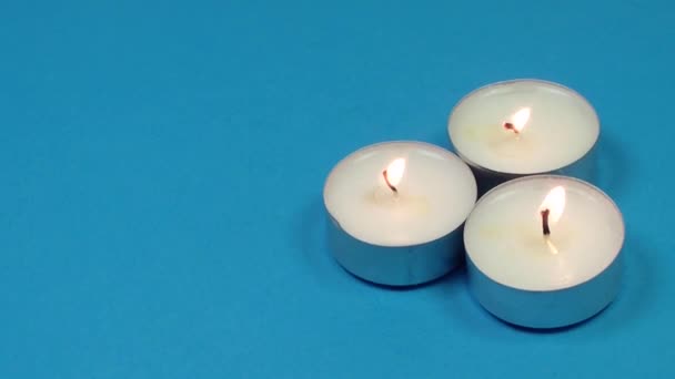 Drei brennende Kerzen - Tabletten rotieren auf blauem Hintergrund. Textraum. — Stockvideo