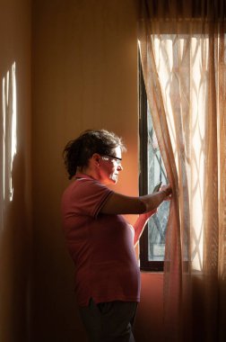  Telefonu pencerenin yanında duran cep telefonu olan kadın. Karantina yüzünden akıllı telefonlu bir kadın evde bekliyor. Son sınıf kadını telefona bakıyor. Yalnız konsept. Karantina