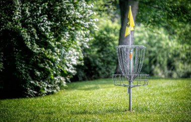 Yeşil çimlerin üzerinde arka planda ağaçlar olan bir disk golf deliği..
