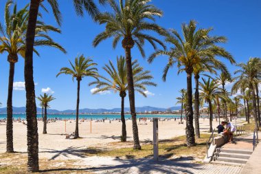 Palmiye ağaçları ve güneşlenen insanlarla S 'Arenal plajı. El Arenal, İspanya 'nın Balear Adaları' nda Mallorca adasına bağlı bir şehirdir..
