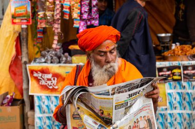 Prayagraj, Uttar Pradesh, Hindistan - Şubat 2019: Hint naga sadhu en büyük Hindu festivalinde gazete okuyor - Kumbh Mela Fair.
