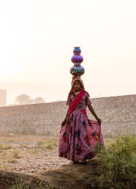 Pushkar, Rajasthan / India - November 2019 : Young indian women in traditional dress carrying pots on her head