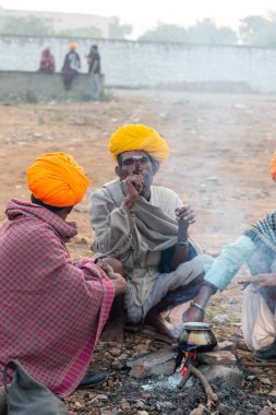Pushkar, Rajasthan / India - November 2019 : Rajasthan people smoking chilam in group at pushkar fair ground with camels in background