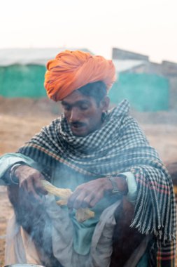 Pushkar, Rajasthan / India - November 2019 : Rajasthan people smoking chilam in group at pushkar fair ground with camels in background