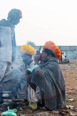Pushkar, Rajasthan / India - November 2019 : Rajasthan people smoking chilam in group at pushkar fair ground with camels in background