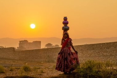 Pushkar, Rajasthan / India - November 2019 : Young carrying pots on her head to attract tourist at camel fair during sunrise