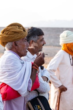 Pushkar, Rajasthan / India - November 2019 : Portrait of camel traders participating with their camels in pushkar camel fair in traditional white rajasthani dress and colorful pagadi (Turban) on their head 