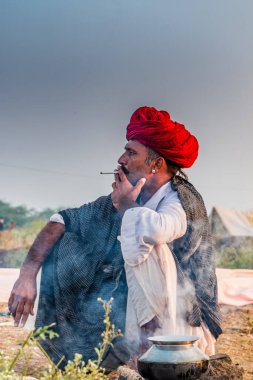 Pushkar, Rajasthan / India - November 2019 : Portrait of camel traders participating with their camels in pushkar camel fair in traditional white rajasthani dress and colorful pagadi (Turban) on their head 