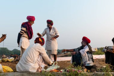 Pushkar, Rajasthan / India - November 2019 : Portrait of camel traders participating with their camels in pushkar camel fair in traditional white rajasthani dress and colorful pagadi (Turban) on their head 