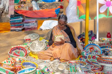 FARIDABAD, HARYANA / INDYA - Şubat 2020: Surajkund Craft Mela 'daki dükkanında el işi sepetleri ve maskeler takan yaşlı Hintli kadın